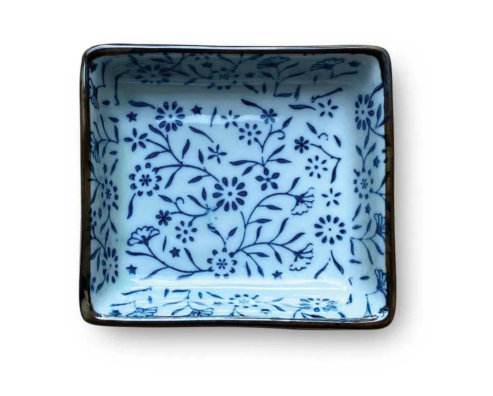 A blue-and-white floral ceramic sauce tray with a dark rim